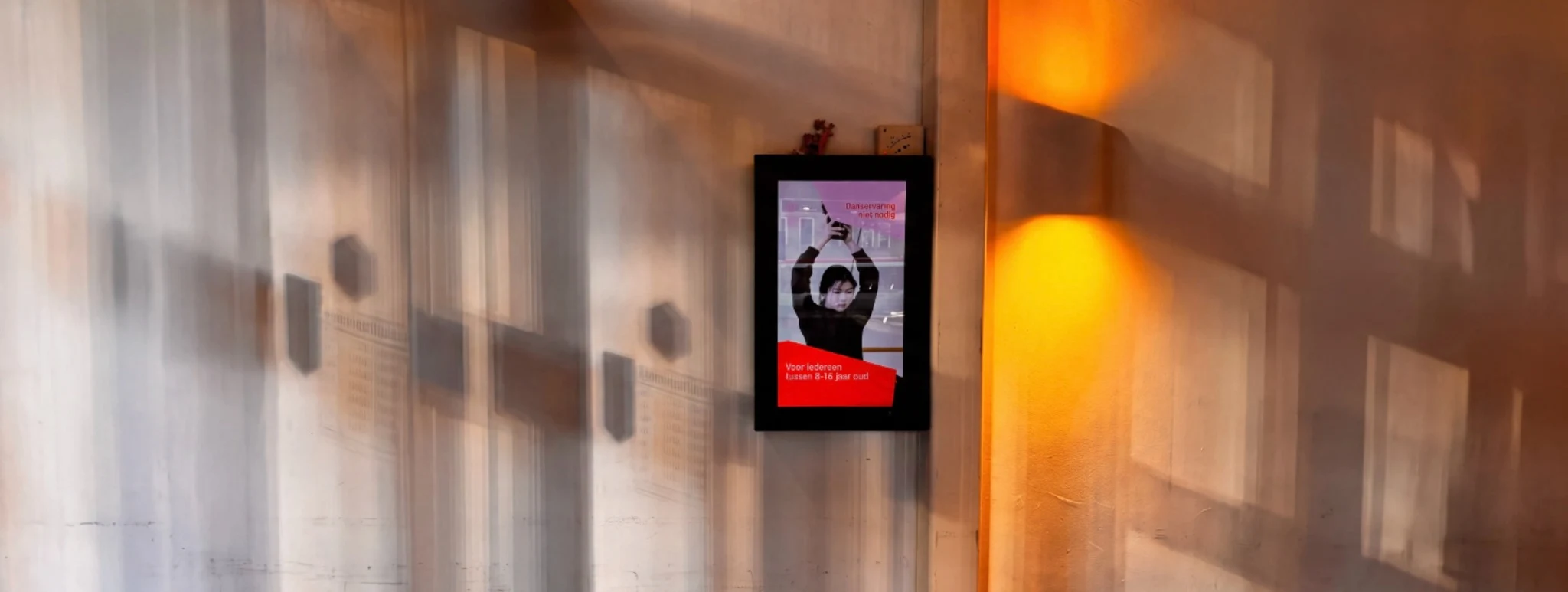 KlikClick-scherm aan een wand met warme lichtval en lange schaduwen